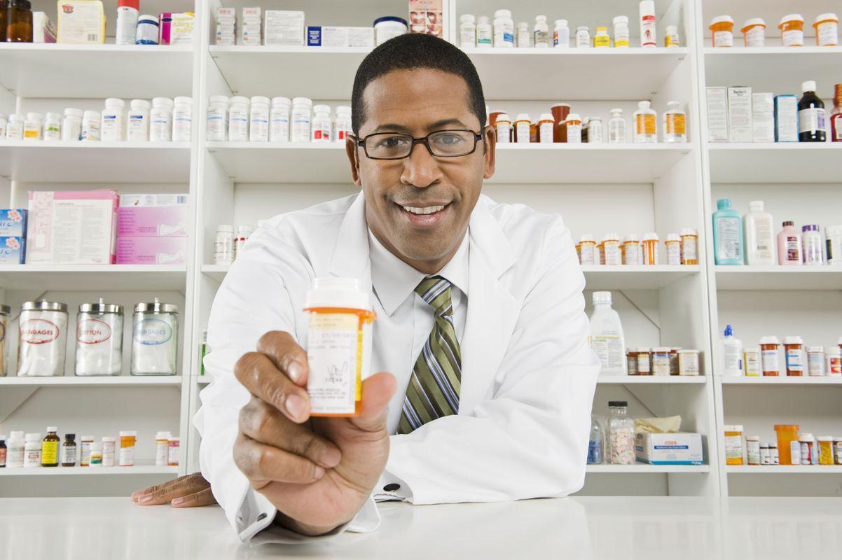 A black male pharmacist holding out a medication.
