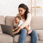 Busy black woman. Child in hand while working on a laptop